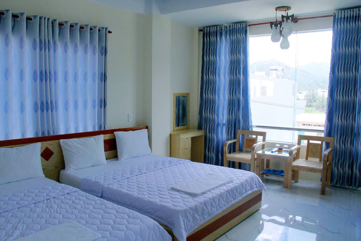 A hotel room with two beds, a desk, a chair, and a view of the outdoors.