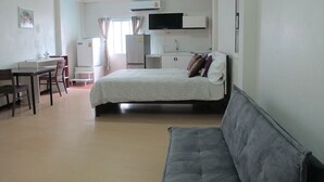 Un dormitorio con cama, escritorio, silla, televisor y kitchenette.
