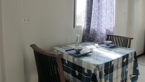 Un comedor con una mesa de vidrio, mantel a cuadros azul y blanco, dos sillas, un tazón, una taza y un jarrón.