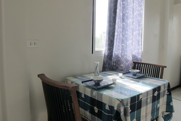 Un comedor con una mesa de vidrio, mantel a cuadros azul y blanco, dos sillas, un tazón, una taza y un jarrón.