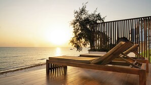 Una terraza de madera con una silla de descanso y vista al océano al atardecer.
