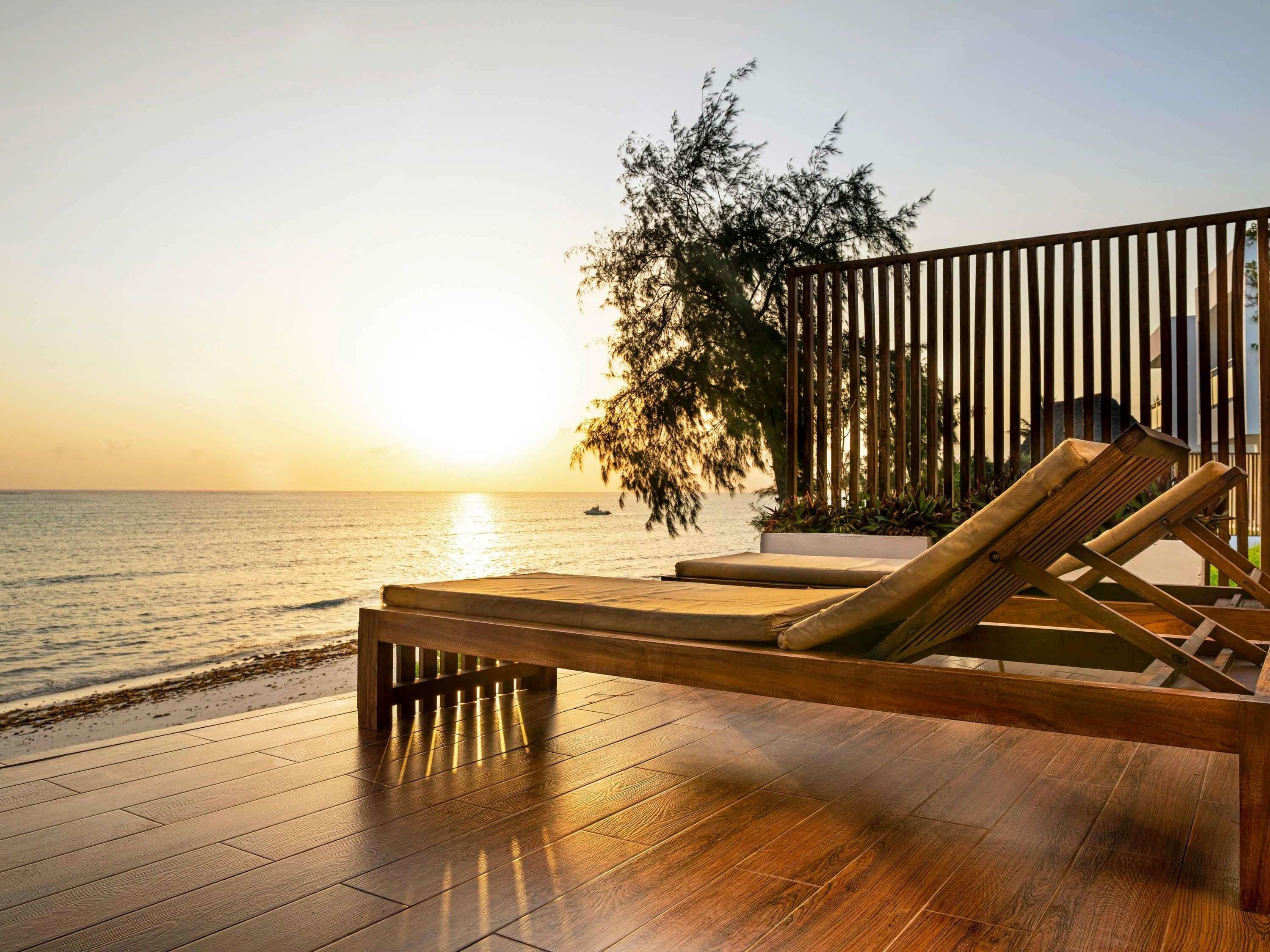 Una terraza de madera con una silla de descanso frente a un cuerpo de agua al atardecer.