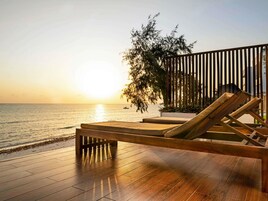 A wooden deck with a lounge chair facing a body of water at sunset.