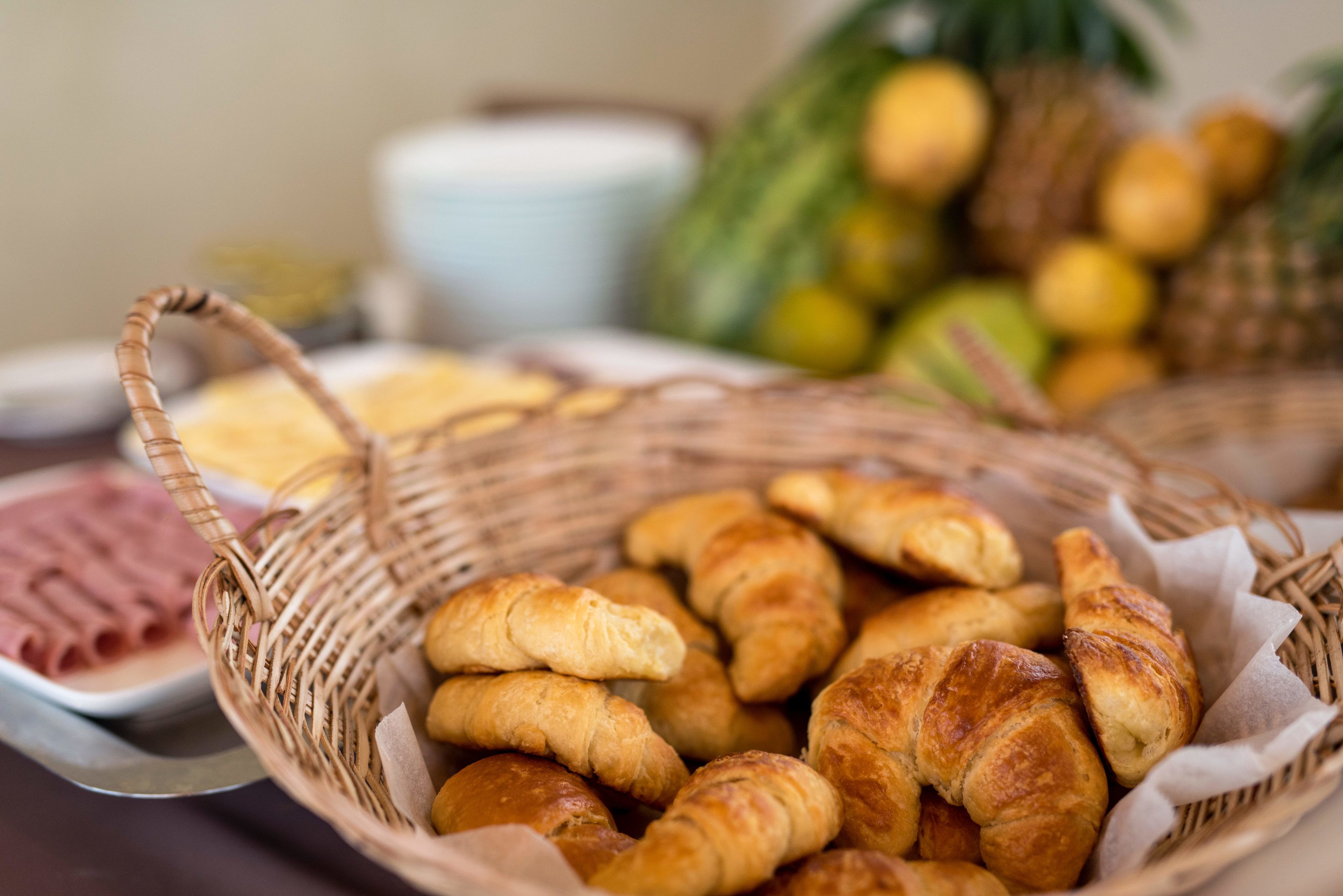 A basket of croissants and ham on a table.