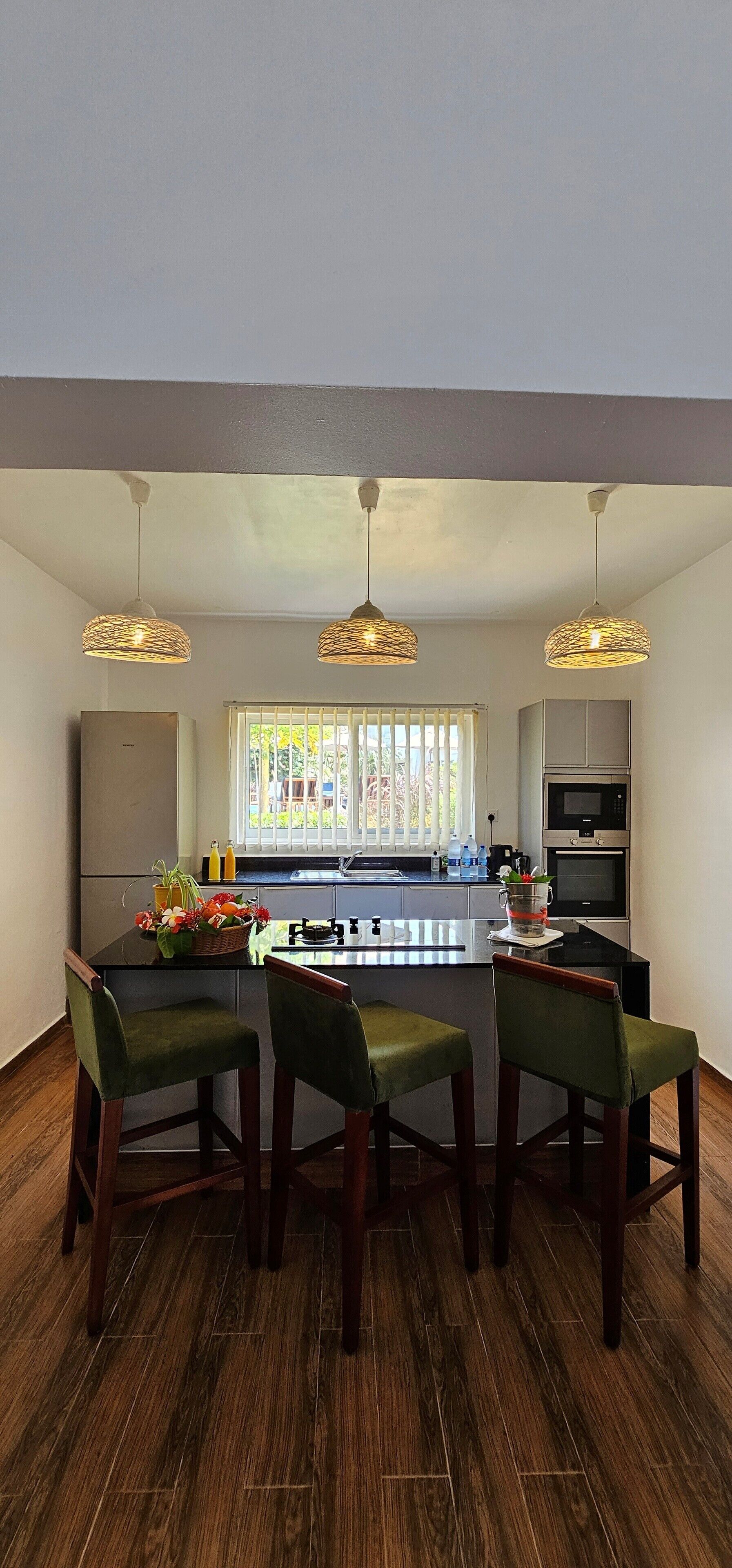 A modern kitchen with a central island, wooden flooring, and pendant lighting.