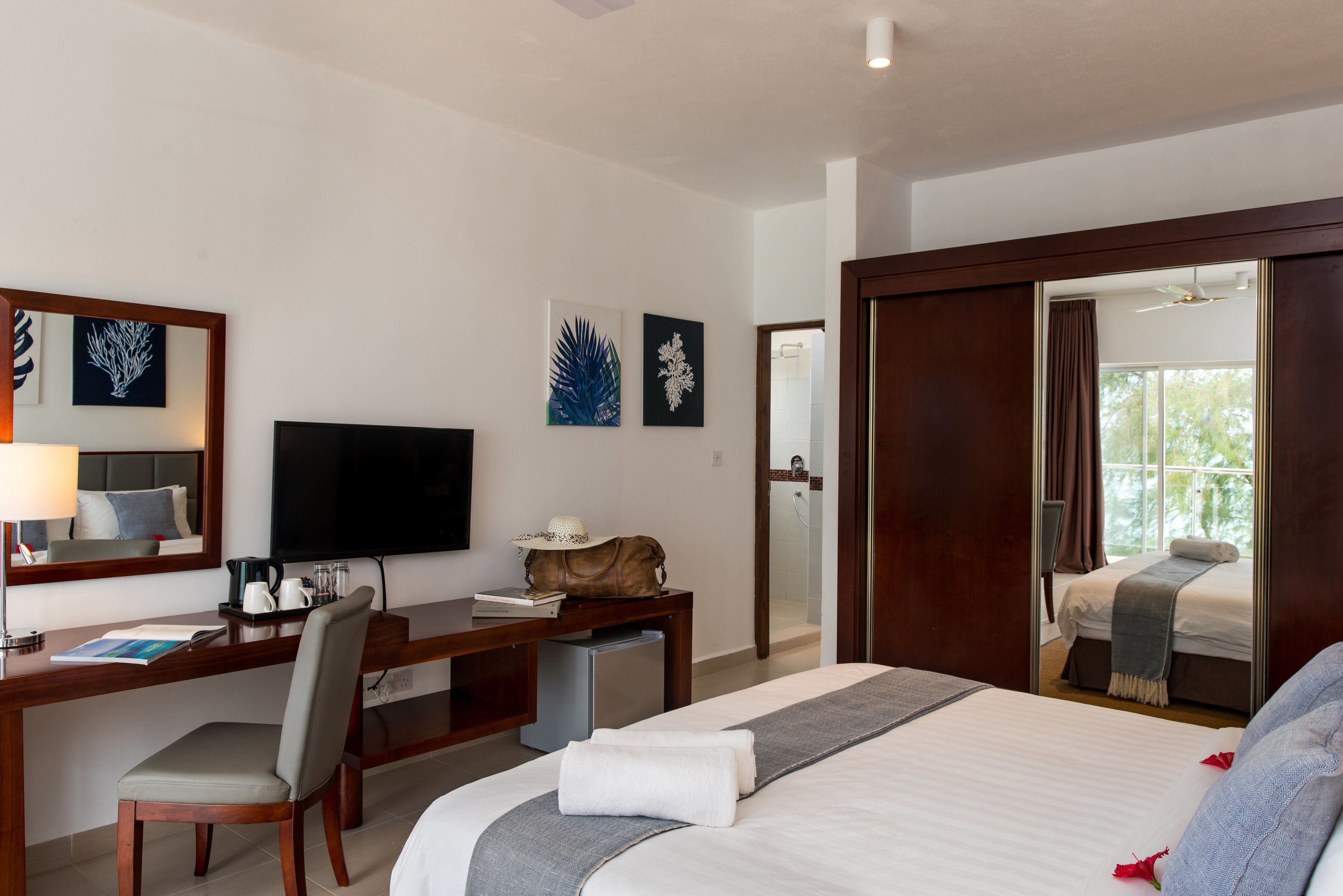 A hotel room with a bed, desk, chair, TV, and artwork on the wall.
