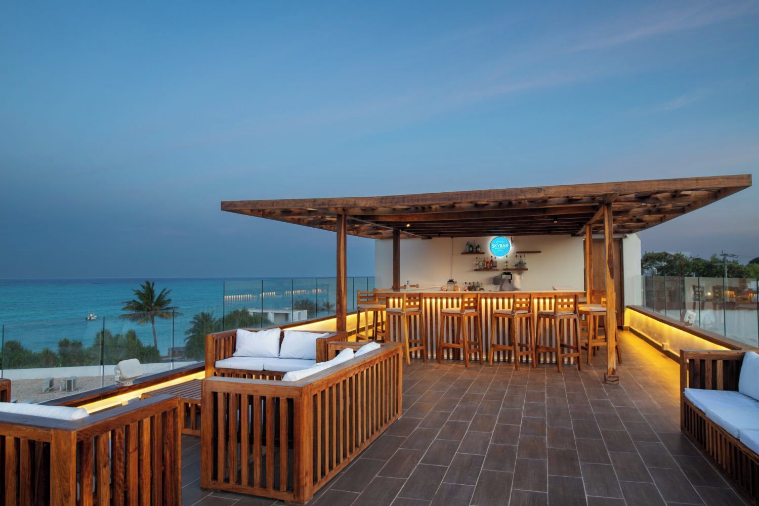 A rooftop bar with wooden furniture, a bar counter, and a view of the ocean.