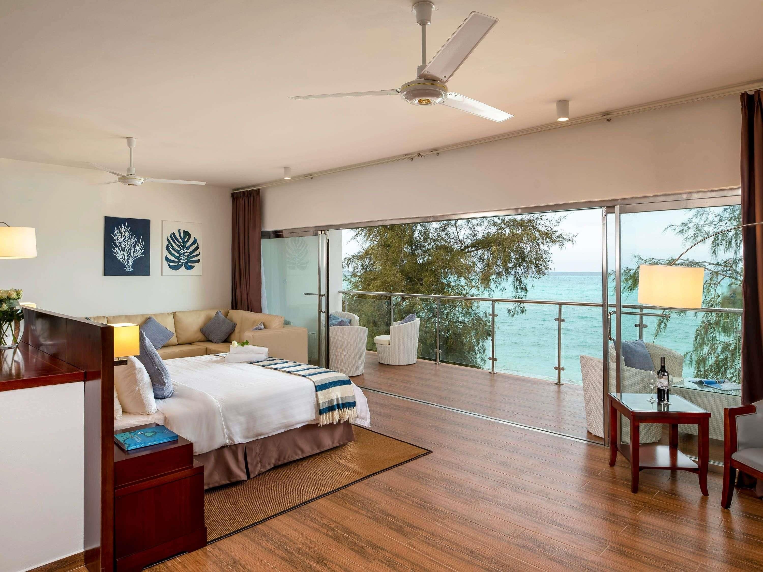 Un dormitorio moderno con una cama grande, un balcón con vistas al mar y un ventilador de techo.