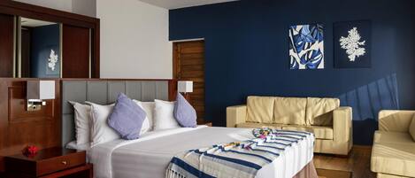 A hotel room with a bed, a sofa, a nightstand, a ceiling fan, and artwork on the walls.