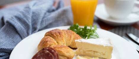 Un plato con cruasanes, queso y salami, un vaso de jugo de naranja y una taza de café sobre una mesa con una servilleta.