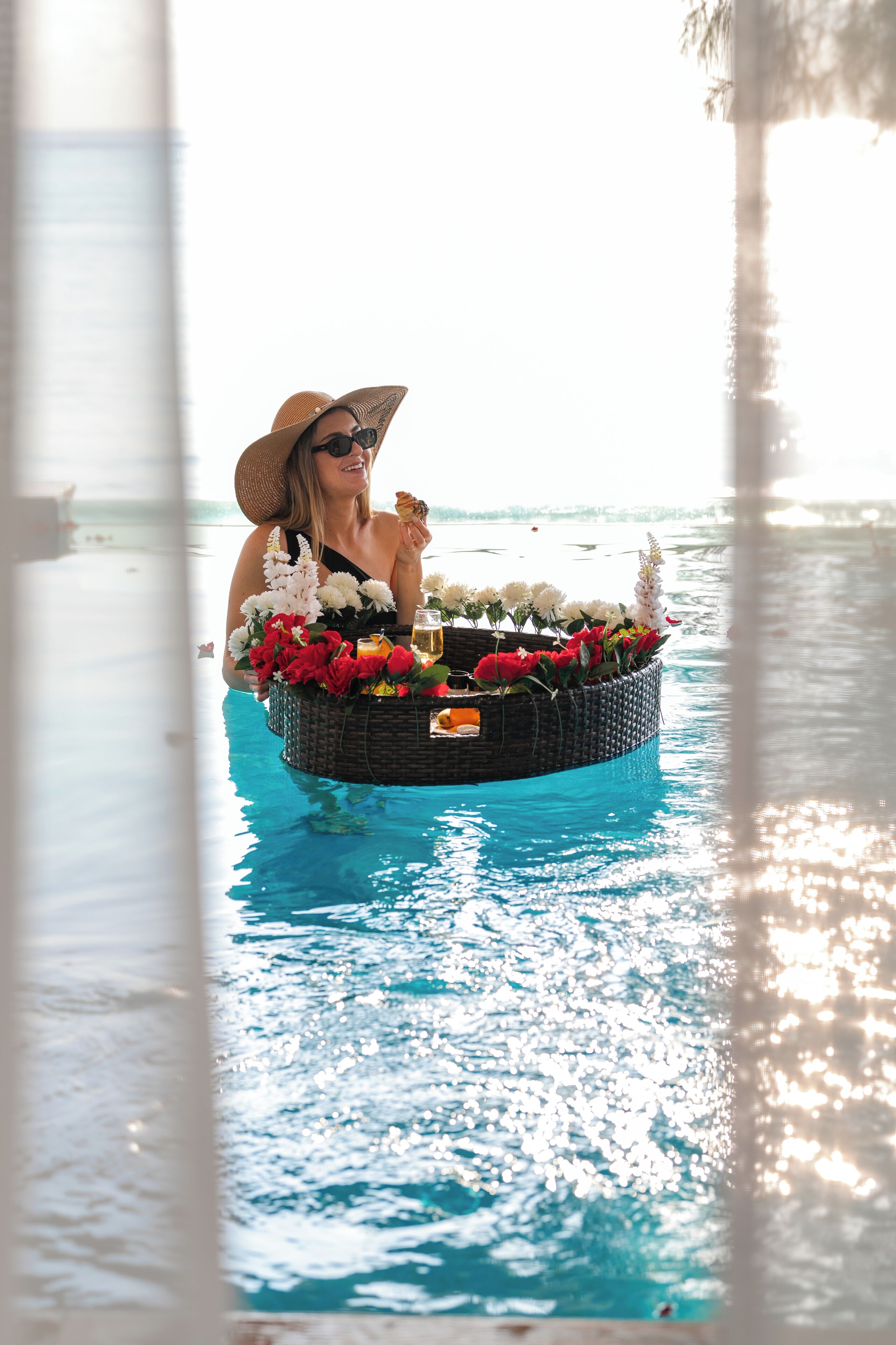 Una persona en una piscina con una cesta flotante que contiene flores y una bebida.