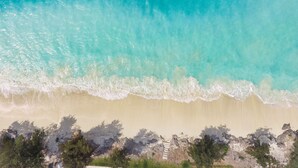 Una playa con agua turquesa cristalina, una orilla arenosa y un promontorio rocoso con una escalera que baja.