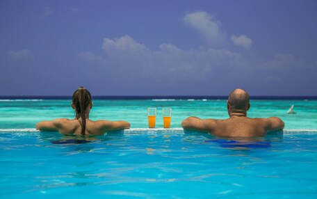 Two people in a swimming pool with a view of the ocean and a clear sky.