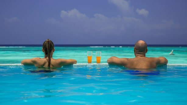 Dos personas en una piscina con vista al océano y un cielo despejado.