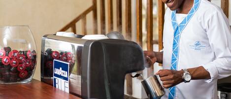 Um barista a servir café numa chávena ao balcão, com uma máquina de café e um copo de vinho tinto.