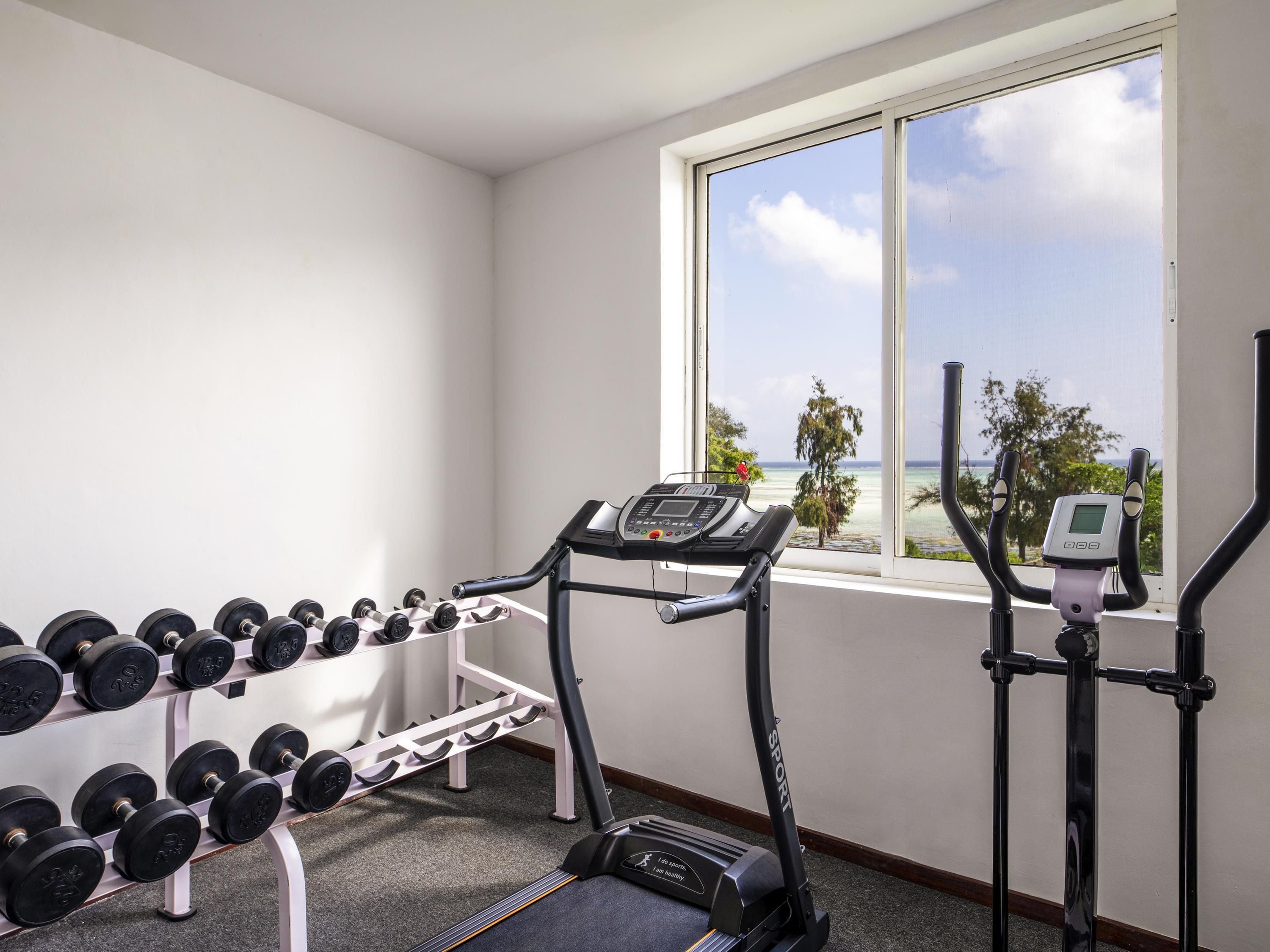 Ein Fitnessstudio mit Laufband, Kurzhanteln und einem Fenster mit Meerblick.