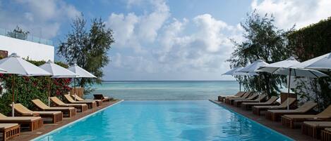 A pool with lounge chairs and umbrellas, overlooking a clear blue sea.