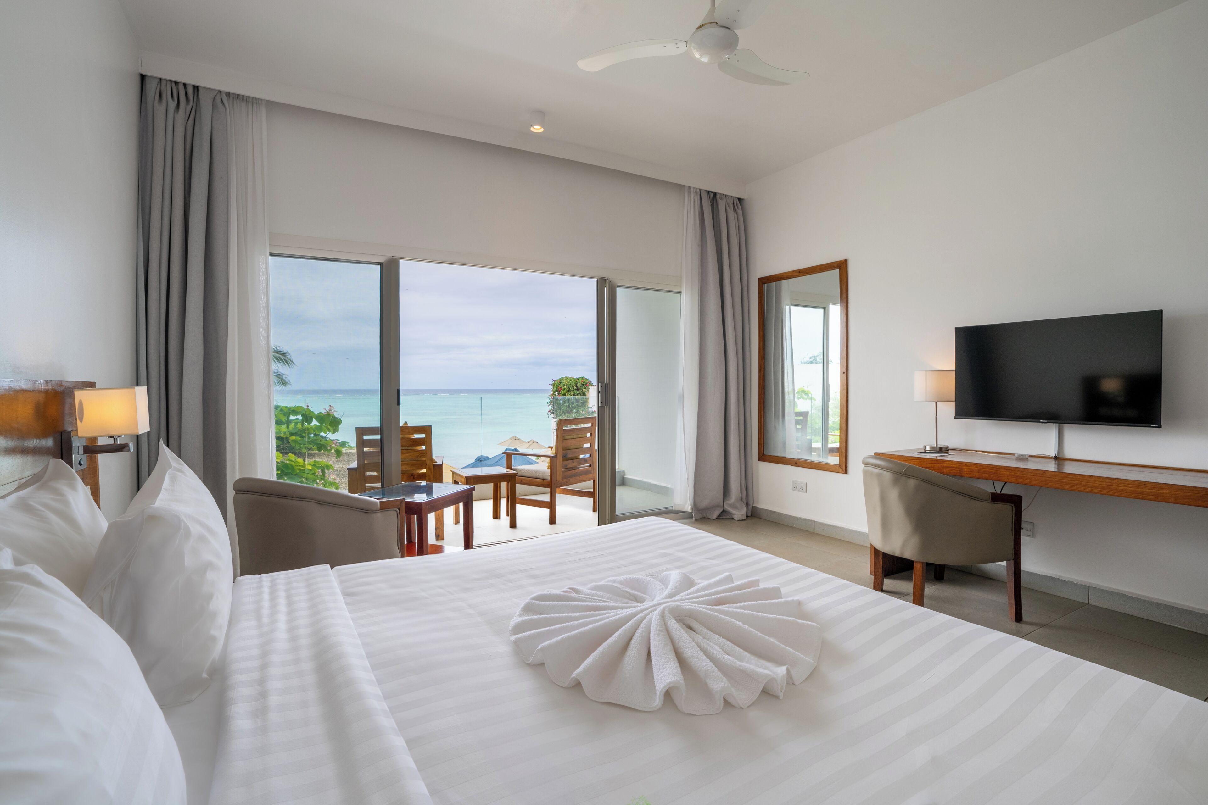 A hotel room with a bed, a desk, a TV, and a view of the ocean.