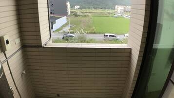 A small, tiled bathroom with a window overlooking a grassy area and buildings.