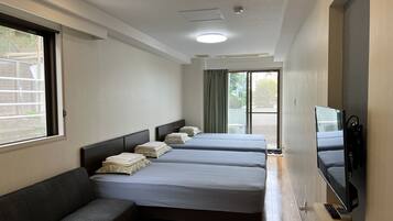 A hotel room with four beds, a sofa, a TV, and a sliding door leading to a balcony.
