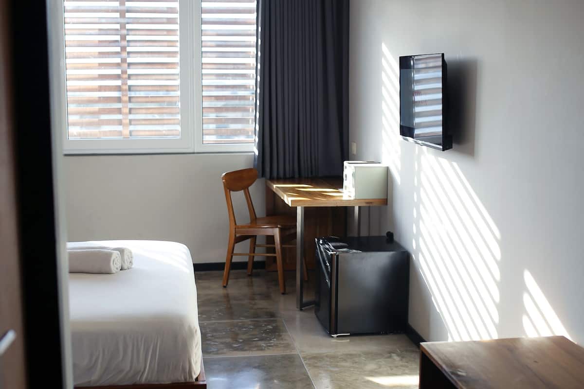Une chambre d’hôtel équipée d’un lit, d’un bureau, d’une chaise, d’une télévision et d’une petite poubelle.