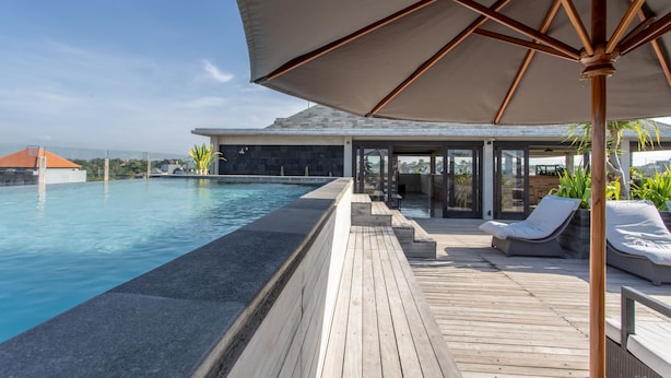 A wooden deck with a pool, lounge chairs, and a covered seating area with a large umbrella. - Surf Motel Canggu (Canggu)