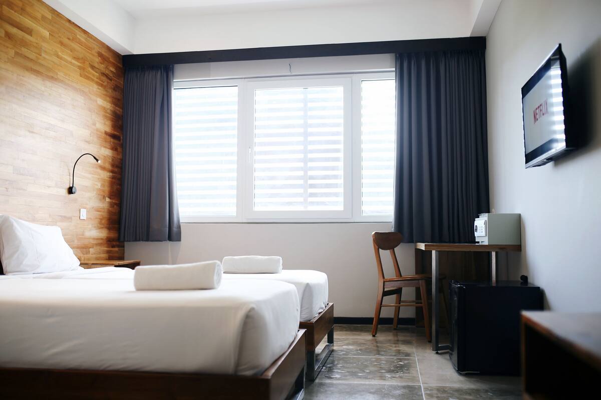 Une chambre d’hôtel avec un mur d’accent en bois, un lit avec du linge de maison blanc, un bureau avec un ordinateur et un téléviseur fixé au mur.