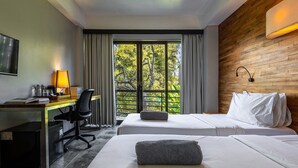 A hotel room with two beds, a desk with a computer, a chair, and a large window with curtains. - Surf Motel Canggu (Canggu)