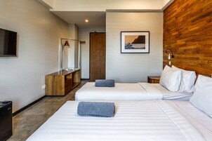 Habitación de hotel con dos camas, cabecero de madera, televisor montado, cómoda de madera y un cuadro enmarcado en la pared.