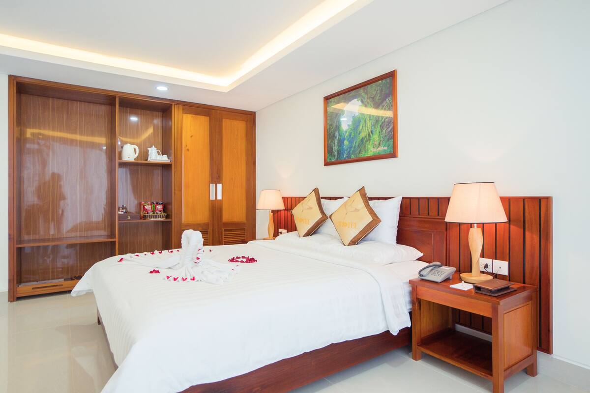Een hotelkamer met een grote houten garderobe, een bed met wit beddengoed, twee bedlampen en een schilderij aan de muur.