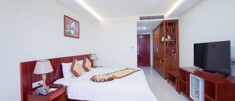 A hotel room with a wooden bed, bedside tables, a TV, and a mini-fridge.