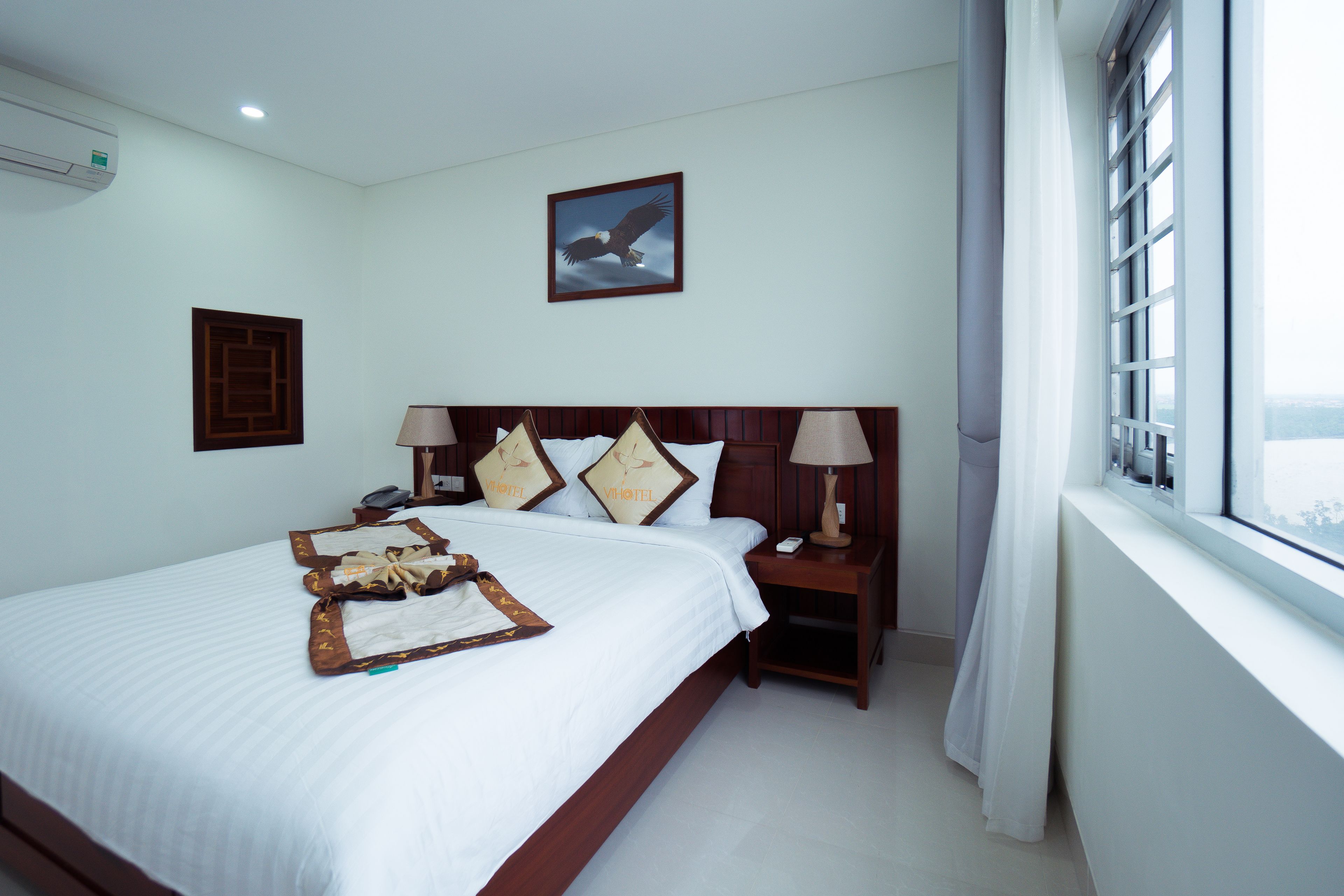 A neatly made bed with a wooden headboard, a bedside table with a lamp, and a framed picture of an eagle on the wall.