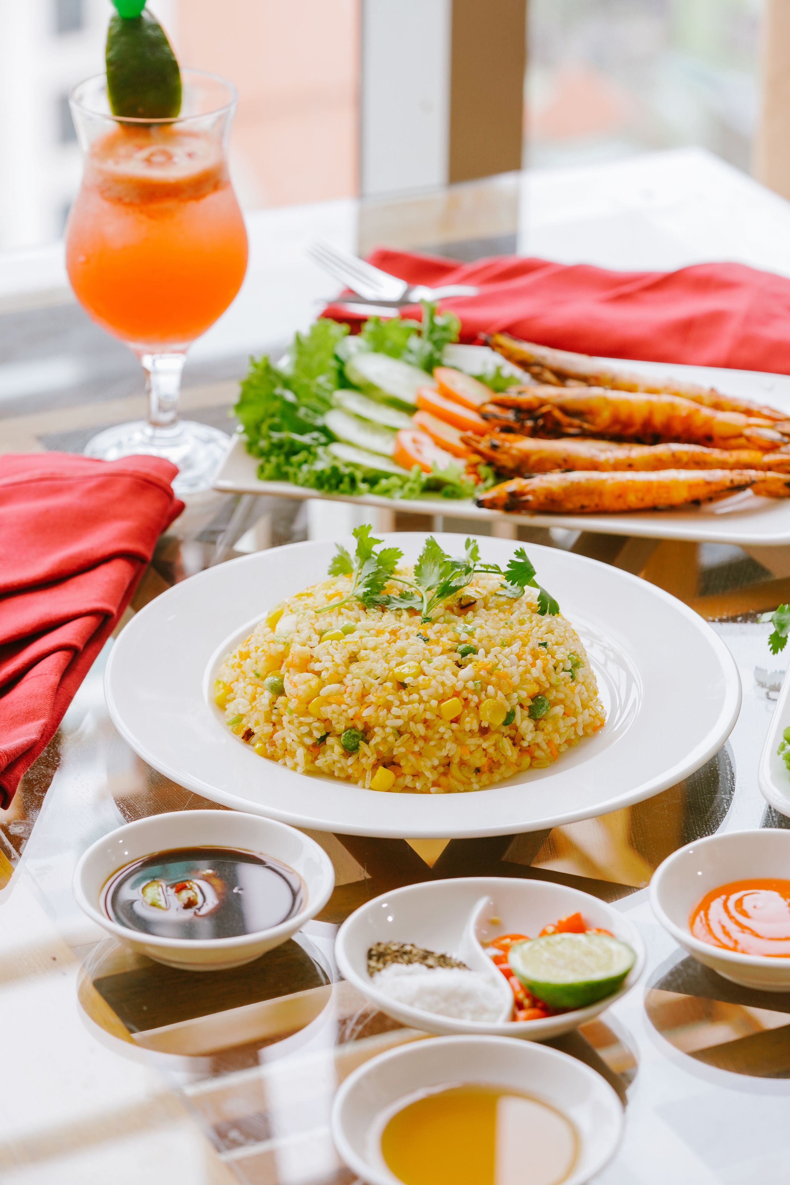 Una mesa con arroz amarillo adornado con hierbas, un vaso de jugo de naranja con un toque de lima y un plato de mariscos a la parrilla.