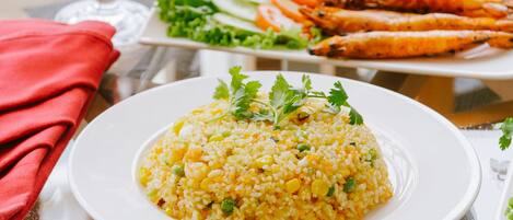 Una mesa con arroz amarillo adornado con hierbas, un vaso de jugo de naranja con un toque de lima y un plato de mariscos a la parrilla.