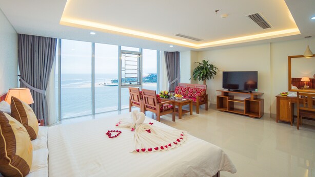 A hotel room with a large bed, a TV, a desk with a chair, and a view of the ocean. - Vinh Hoang Hotel (Dong Hoi)