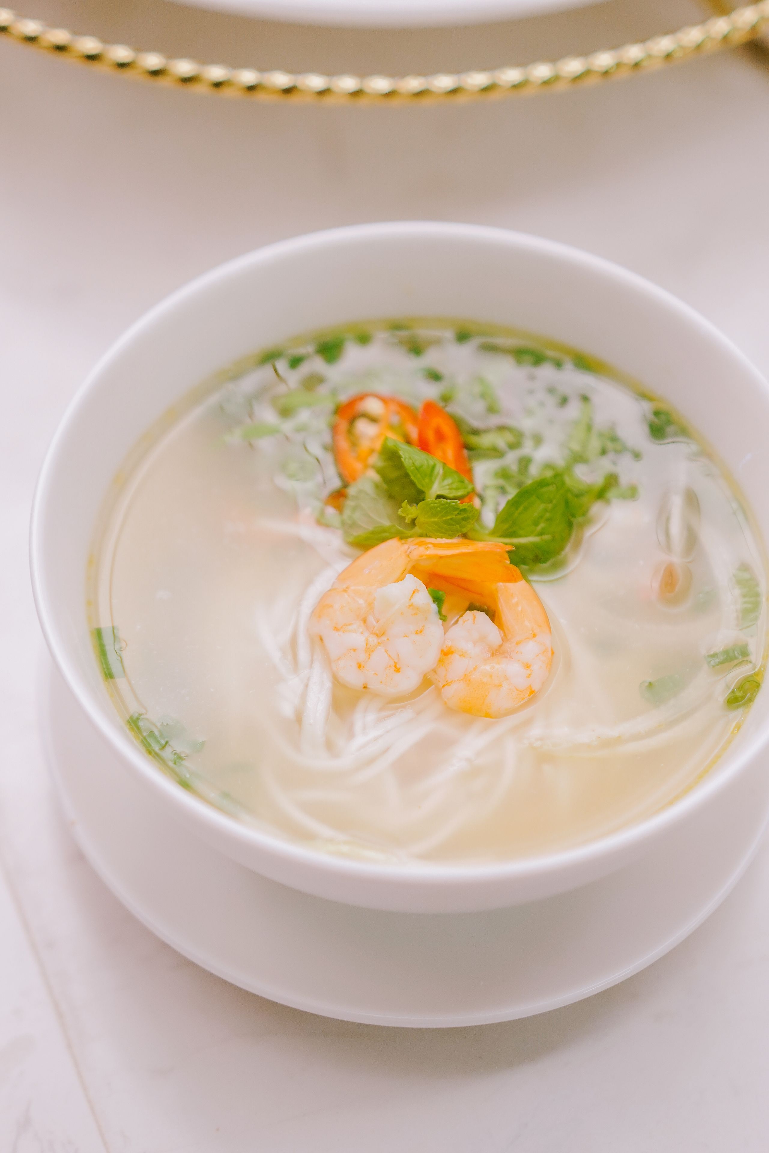 A bowl of soup with noodles, shrimp, and vegetables.