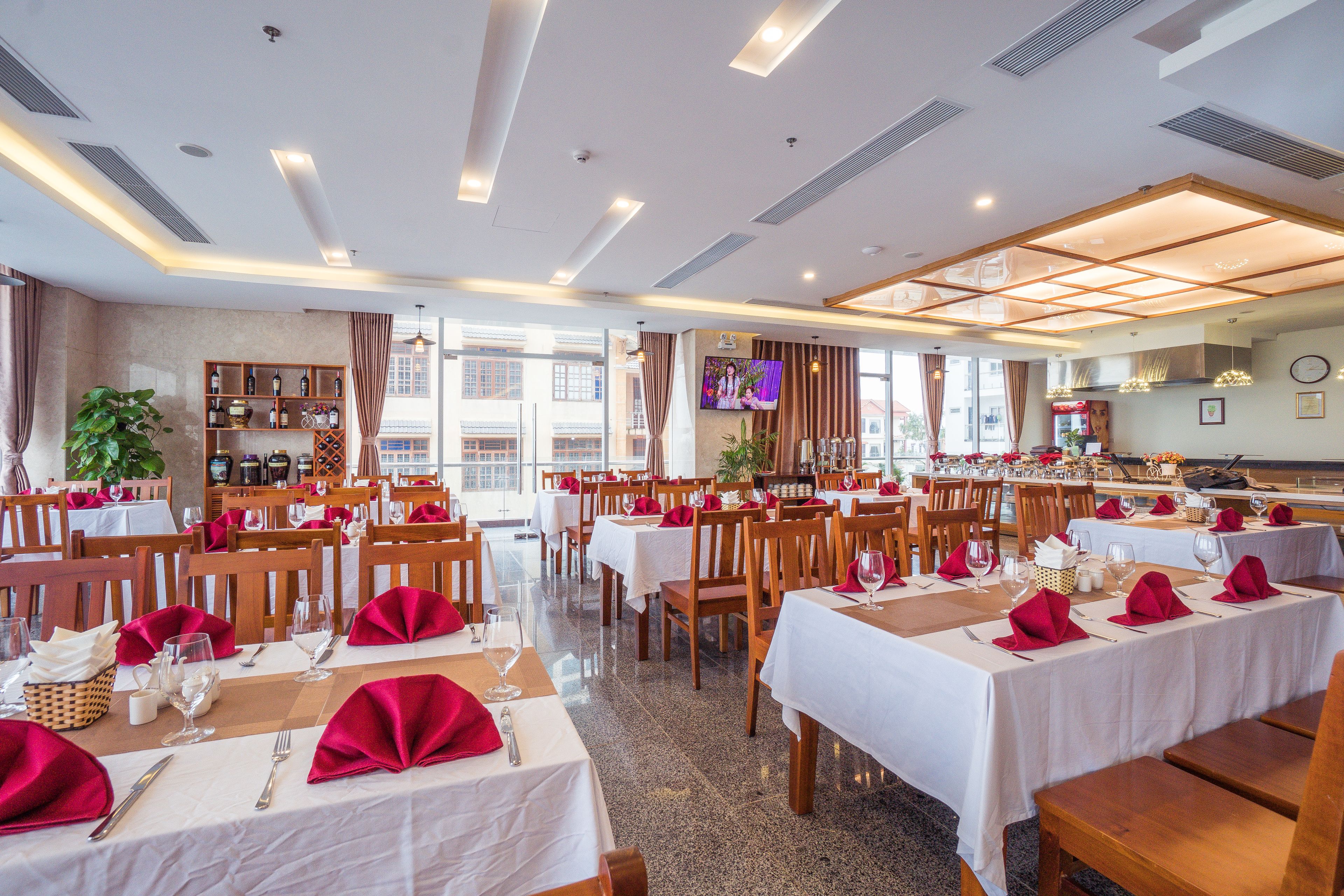 Uma sala de jantar com mesas preparadas para vários convidados, com toalhas brancas e guardanapos vermelhos.