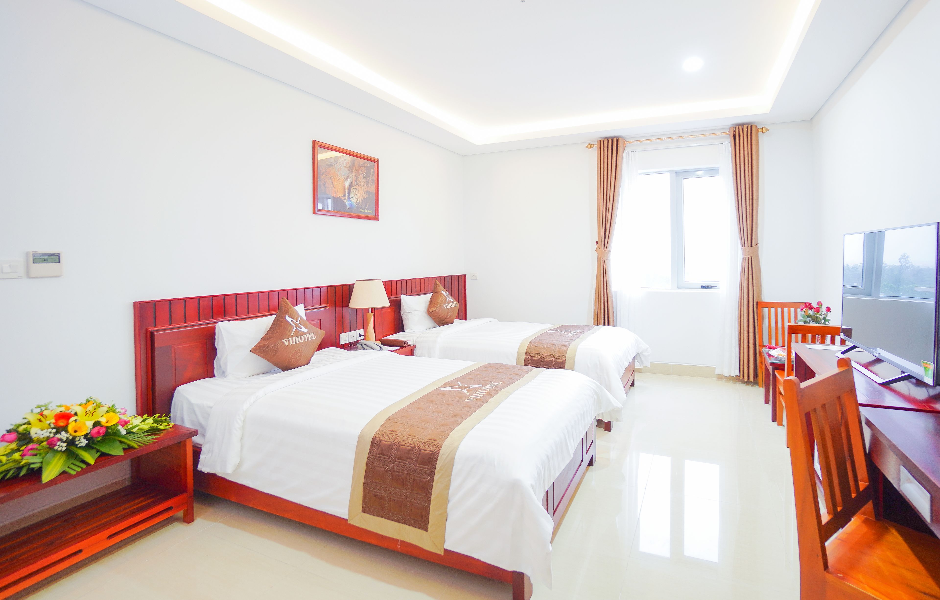 A hotel room with two beds, a desk, a TV, and a window with curtains.