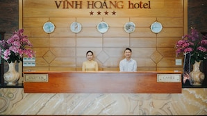 A reception desk at Vinh Hoang hotel with a wooden panel design, clocks, and vases of flowers. - Vinh Hoang Hotel (Dong Hoi)