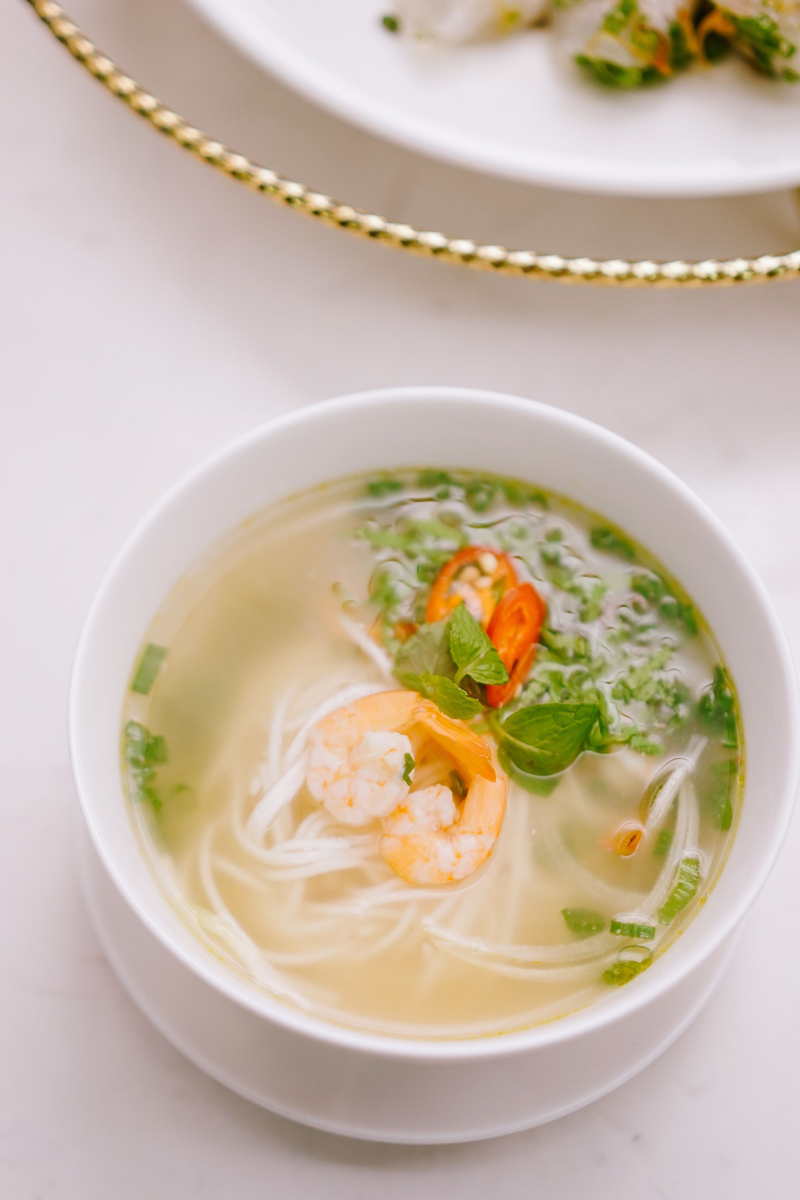 A bowl of soup with noodles, shrimp, and herbs.