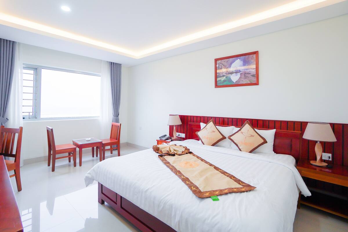 Een hotelkamer met een groot bed, een bureau, stoelen, een raam en een schilderij aan de muur.