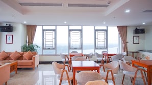 A spacious room with a sofa, chairs, tables, and large windows offering a view. - Vinh Hoang Hotel (Dong Hoi)