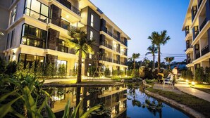 Un hotel moderno con varios balcones, una fuente central y jardines bien cuidados.