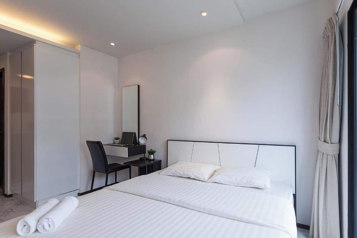 Ein modernes Hotelzimmer mit einem großen Bett, einem Schreibtisch mit Computer, einem Sessel und einem Spiegel.