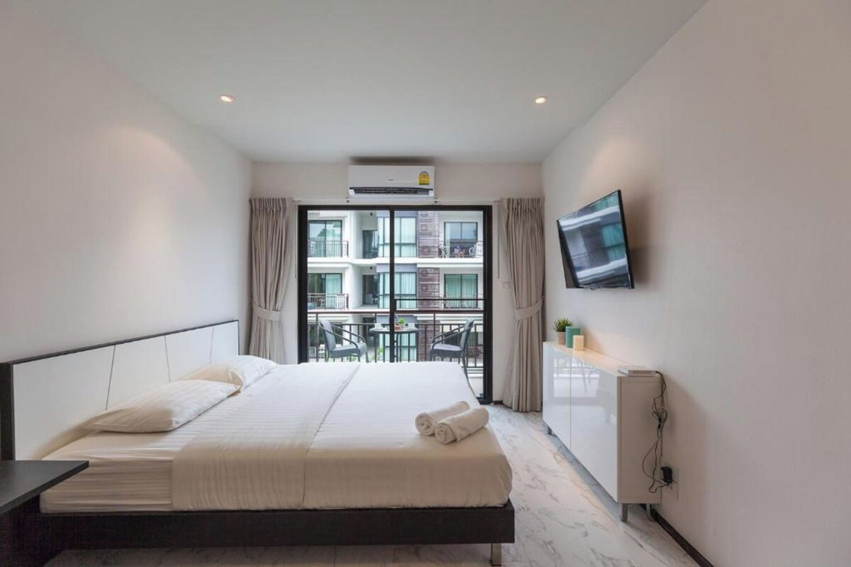 A hotel room with a bed, a TV, a desk, and a window with a view of buildings.