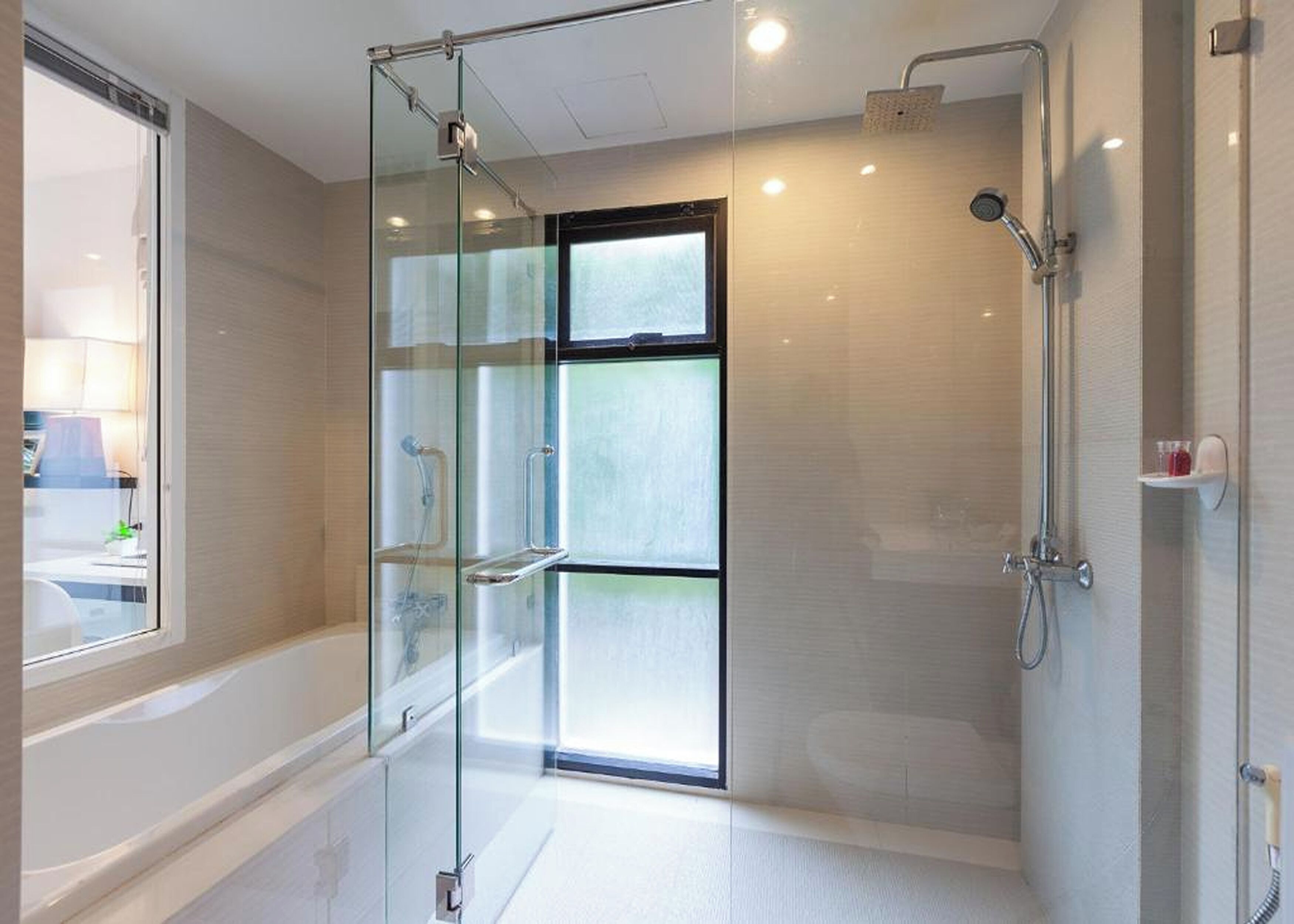 Een moderne badkamer met een douchecabine van glas, een zichtbaar raam en een douchekop.