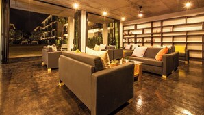 Un área de estar moderna con sofás y una estantería, que presenta un techo de concreto y ventanas amplias.