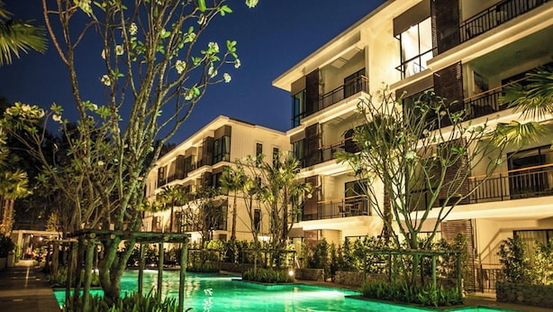 Un hotel de varios pisos con piscina, rodeado de abundante vegetación y palmeras.