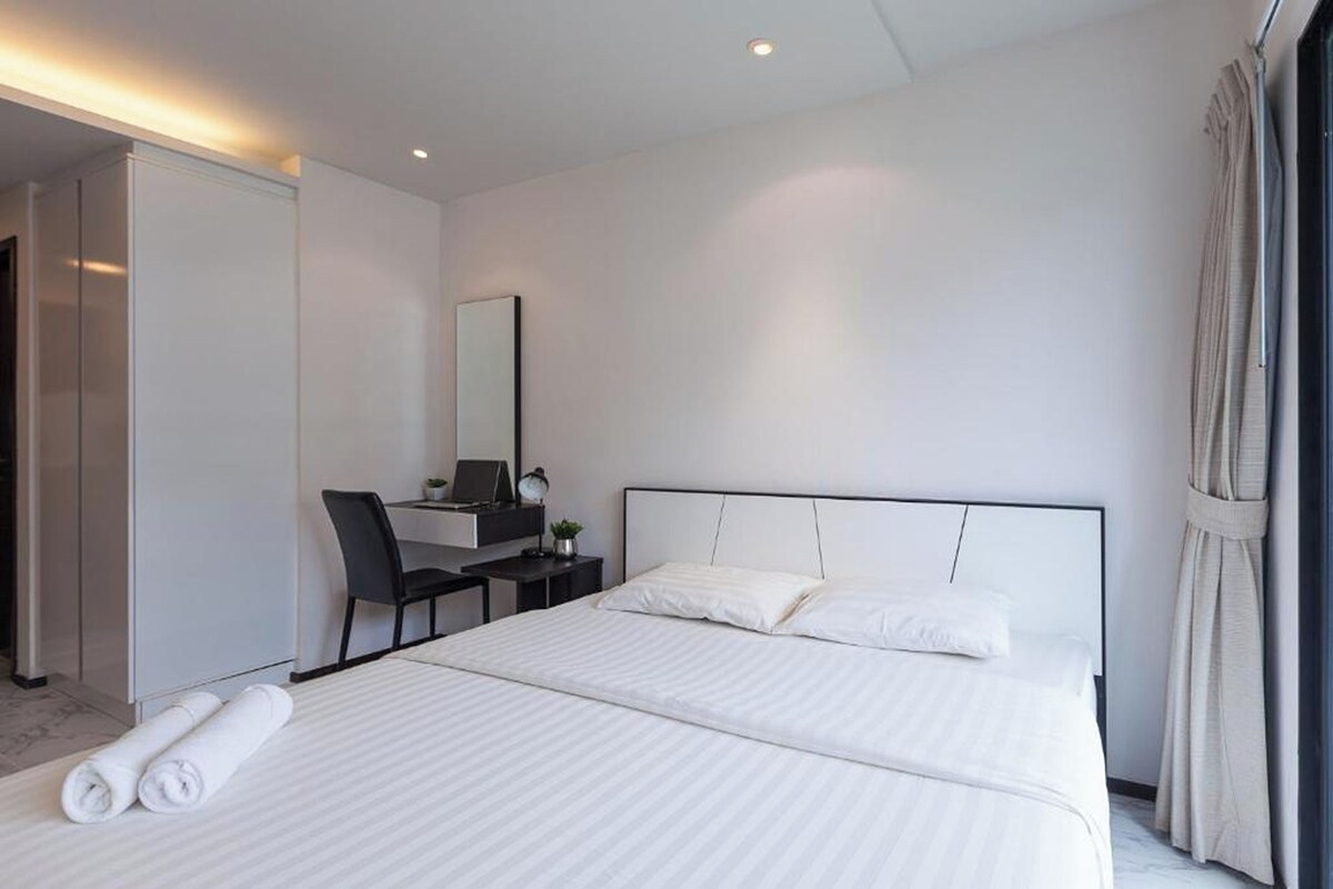 Una habitación de hotel moderna con una cama grande, un escritorio con silla, un espejo y una ventana con cortinas.
