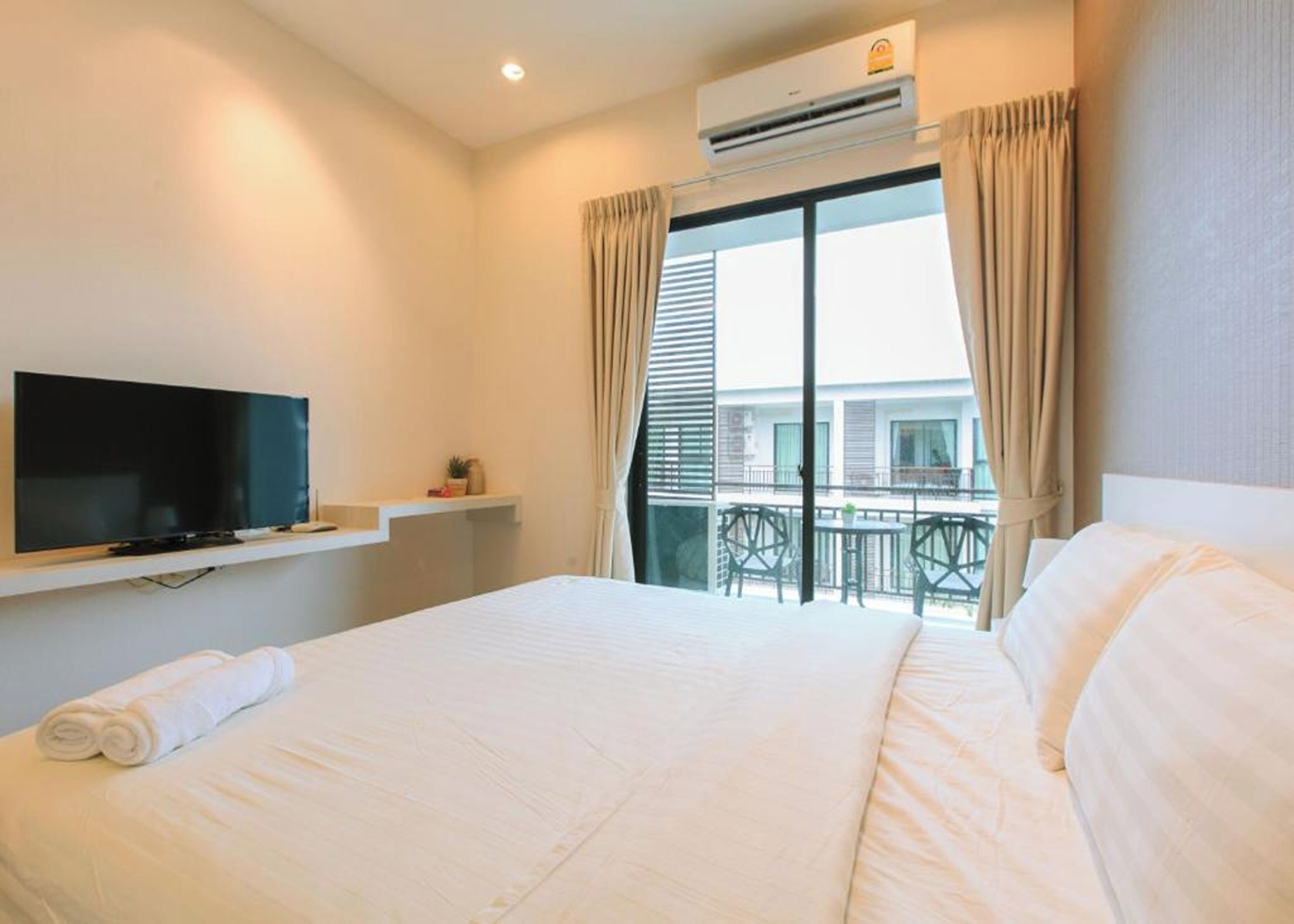 A hotel room with a bed, a TV, an air conditioner, and a balcony with outdoor furniture.